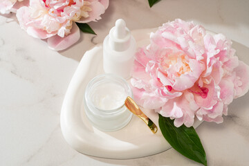 Serum dropper bottle and cream jar on a concrete tray with pink peonies. Urban-meets-natural...