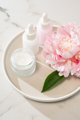 Pink peonies, glass serum dropper, and cream jar arranged on a concrete tray. chic beauty still life for minimalist branding