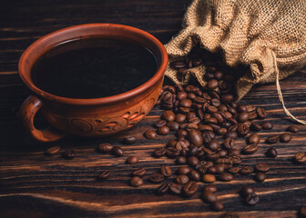 Cup of black coffee and spilled roasted beans from burlap sack on wooden table