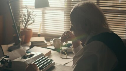 Side view shot of senior Caucasian male author sitting in front of vintage typewriter dealing with writers block and then starting typing having inspiring idea for his new novel