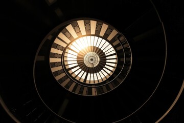 Obraz premium Spiral staircase with dramatic skylight and warm sunlight streaming through, abstract architectural perspective viewed from below, vintage ironwork details, radial symmetry and elegant classic design 