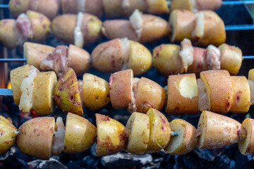 Potatoes with lard are grilled on a skewer over open flames, creating a rustic and flavorful...
