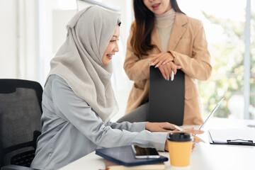 Asian and Muslim girls working together on a laptop.
