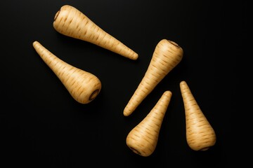 Juicy, freshly harvested parsnips displayed on a dark surface, overhead shot with space for message