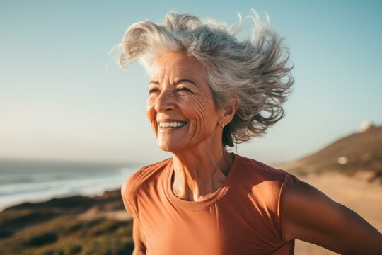 Senior woman with gray hair enjoying a healthy lifestyle, running on the beach with the wind in her hair