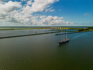 A majestic sailing ship glides across calm waters under a partly cloudy sky, with coastal...