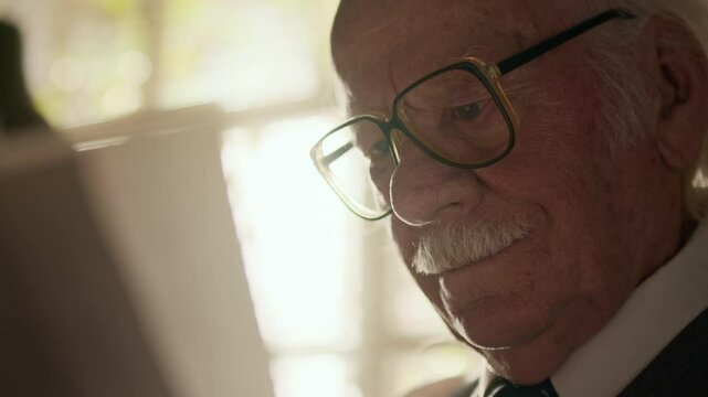 Close up shot of focused elderly Caucasian man in retro eyeglasses studying paper documents or script by window