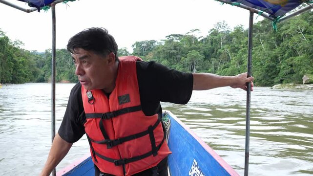 Tourist wearing bright orange life jacket cruising along Misahualli River, surrounded by lush Amazon rainforest greenery during scenic tropical adventure in Ecuadorian wilderness