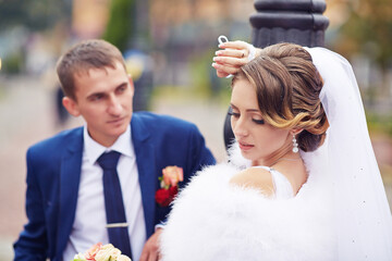 A bride and groom are sitting on a bench, the bride is wearing a white dress