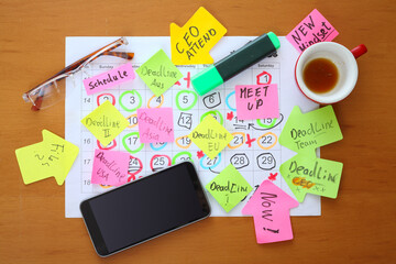 Calendars with business appointments, deadline notice and adhesive notes on cluttered desk....