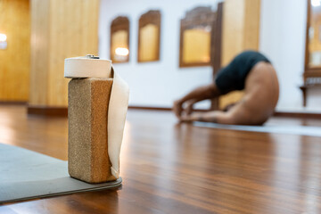 Yoga cork block and strap on floor with blurry man stretching in background
