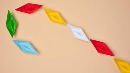 Multi-colored origami paper boats are arranged in a curved line, symbolizing a path or connection
