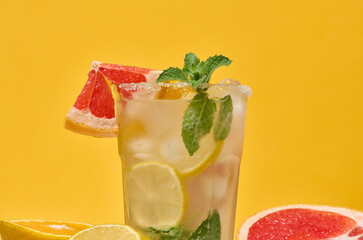 Close up of a glass with a cold drink garnished with a grapefruit slice on the rim and mint, ice...
