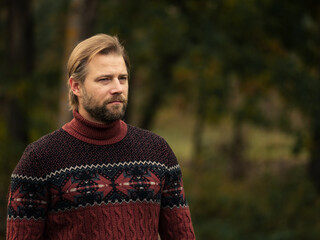 Portrait of handsome young man in wool knitted sweater outdoors. Male with long hair and beard feel...