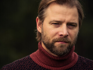 Portrait of handsome young man in wool knitted sweater outdoors. Male with long hair and beard feel happy, calm and serious on Green nature background. Man looking away into distance. Diversity People