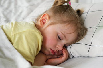 Peaceful adorable baby sleeping on a bed at home. Slumbering little child. Two years old girl sleeps peaceful at domestic room interior background. Serene dream. Cute face close up. Deep kid slumber