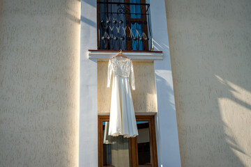 White dress in sunlight. A white dress hangs outside a building, illuminated by sunlight that...