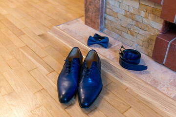 Formal attire laid out before event. Elegant blue shoes, bow tie, and belt arranged on wooden floor...