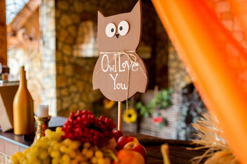 Festive owl decor. A wooden owl sign displays a sweet message amidst colorful fruits and decorative elements in a cozy setting.