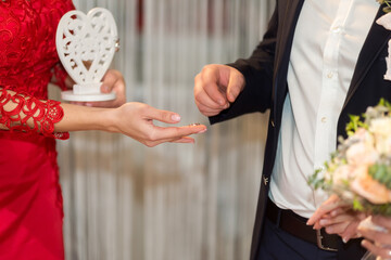 Couple exchanging wedding rings. A bride hands a ring to her groom in a decorated venue, celebrating their commitment during a wedding ceremony.