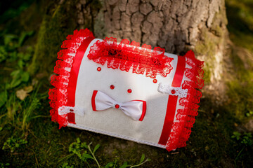 Decorative red and white cushion by tree. A beautifully crafted cushion adorned with red lace and a bow rests against a tree trunk in a tranquil outdoor setting.