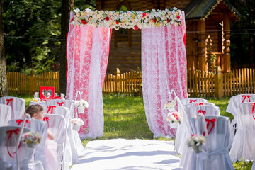 Garden wedding setup outdoors. A lovely wedding altar awaits in a tranquil garden, with elegant white chairs decorated with ribbons.