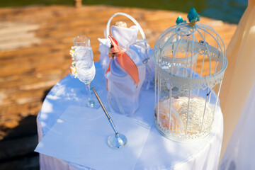 Elegant wedding decor by the lakeside. A beautifully arranged table features a wine bottle, glasses, and a decorative birdcage near a serene lake setting.