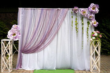 Floral backdrop for outdoor event setup. A beautifully decorated backdrop featuring large flowers and draped fabric, perfect for an outdoor celebration.