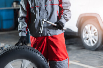 Concept replacement of winter and summer wheels. Mechanic holding tire at repair garage