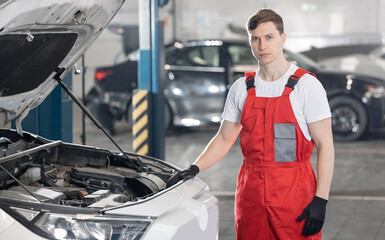Caucasian male auto mechanic in red overalls working on car engine in workshop
