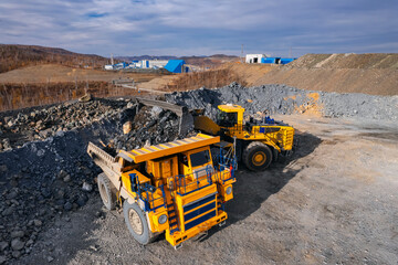 Aerial view excavator loads gold ore rock formation into back of heavy mining dump truck. Concept...