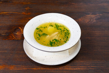 Delicious bowl of clear chicken soup with herbs served on a rustic wooden table