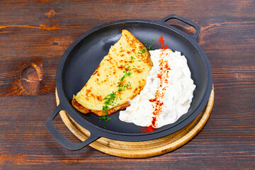Delicious savory omelet served with creamy yogurt sauce and spices on a wooden table