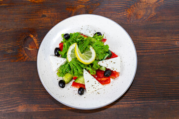 Fresh and vibrant salad with greens, tomatoes, feta cheese, olives, and lemon on a wooden table