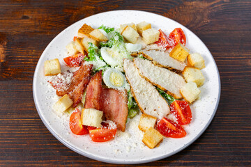 Fresh garden salad topped with grilled chicken, crispy bacon, and croutons served on a white plate
