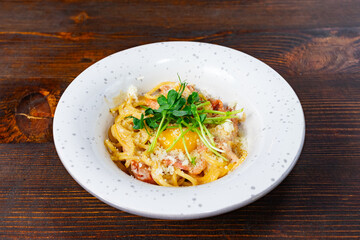 Delicious pasta dish with egg yolk and herbs served in a white bowl on a rustic wooden table