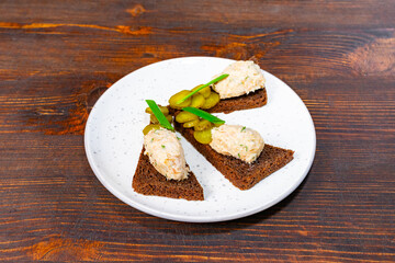 Delicious open-faced sandwiches served on rye bread with a creamy spread and pickles on a rustic wooden table