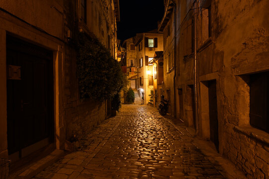 Fototapeta Charming Rovinj alley illuminated at night, with cobblestone streets reflecting the warm glow, inviting exploration of its historic beauty.