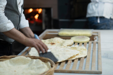 Male hands brushing freshly baked famous flat bread called lavaş in front of a wood burning fire in a traditional bakery in Turkey