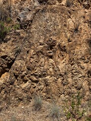 Rocky hillside with sparse dry vegetation and visible strata, showcasing rugged geological formations in a dry Mediterranean climate.