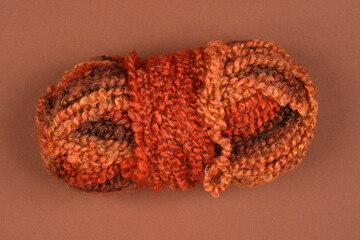 A single skein of multi-colored yarn with rich earthy tones of brown, orange, and beige is presented on a brown background