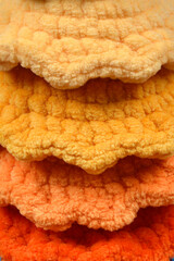 A close-up shot reveals three layers of soft, textured fabric in shades of yellow, orange, and dark...