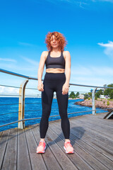 Energetic red-haired curly young woman in sportswear doing stretching exercises.