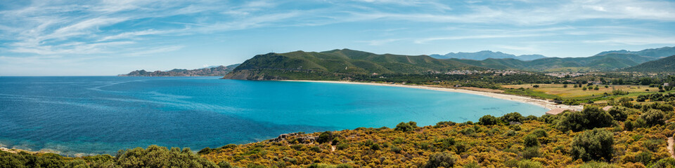 Panoramic view of the white sand beach at Lozari in the Balagne region of the Mediterranean island of Corsica with the Desert des Agriates in the distance
