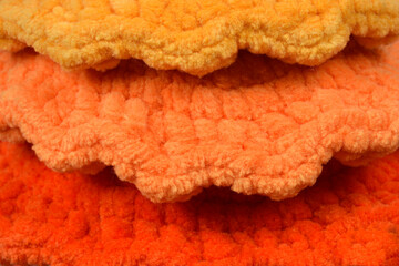 A close-up shot reveals three layers of soft, textured fabric in shades of yellow, orange, and dark orange, arranged in a ruffled pattern