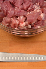 Diced pork pieces in a glass bowl and a knife blade on a wooden cutting board