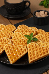 Delicious heart-shaped waffles served with coffee and sugar on a wooden table