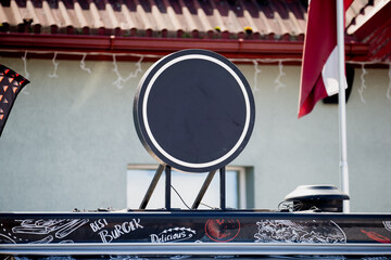 empty round black restaurant sign on street food truck above burger graphics in urban setting...