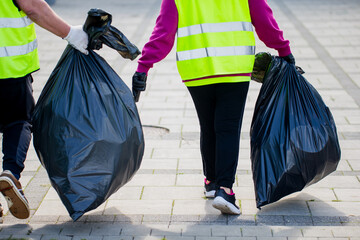 people in reflective safety vests carrying black garbage bags cleaning city streets during...