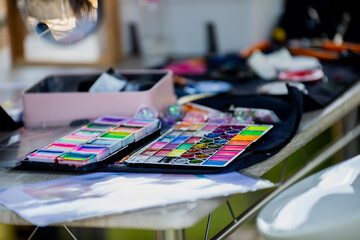 colorful face painting palette on artist table during outdoor event with makeup accessories bright...